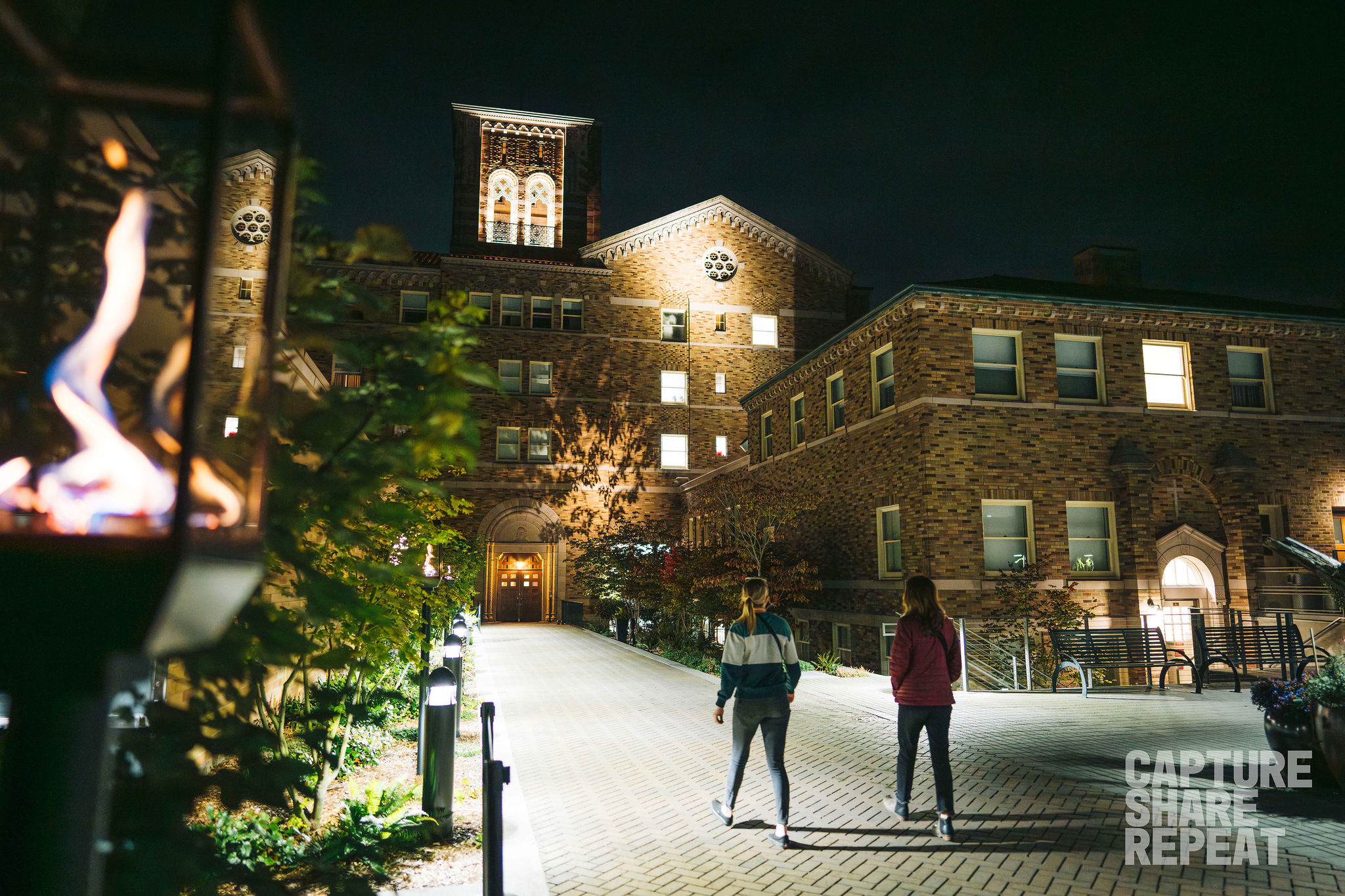 Two women walking on path in front of hotel at night.
