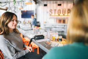 Lady at bar with Stoup sign in background and beverages on the bar.